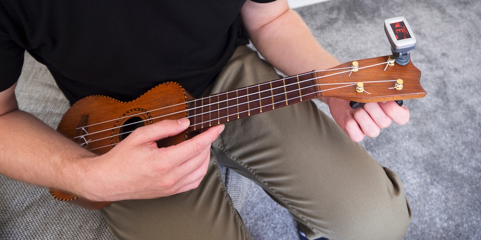 Person stimmt eine Ukulele mittels eines Stimmgerätes