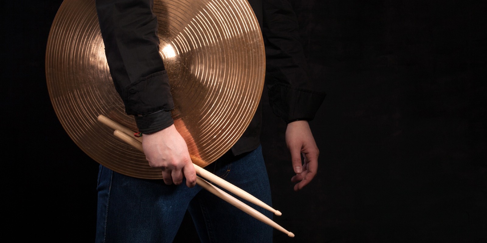 Mann trägt ein Orchesterbecken und ein Paar Sticks