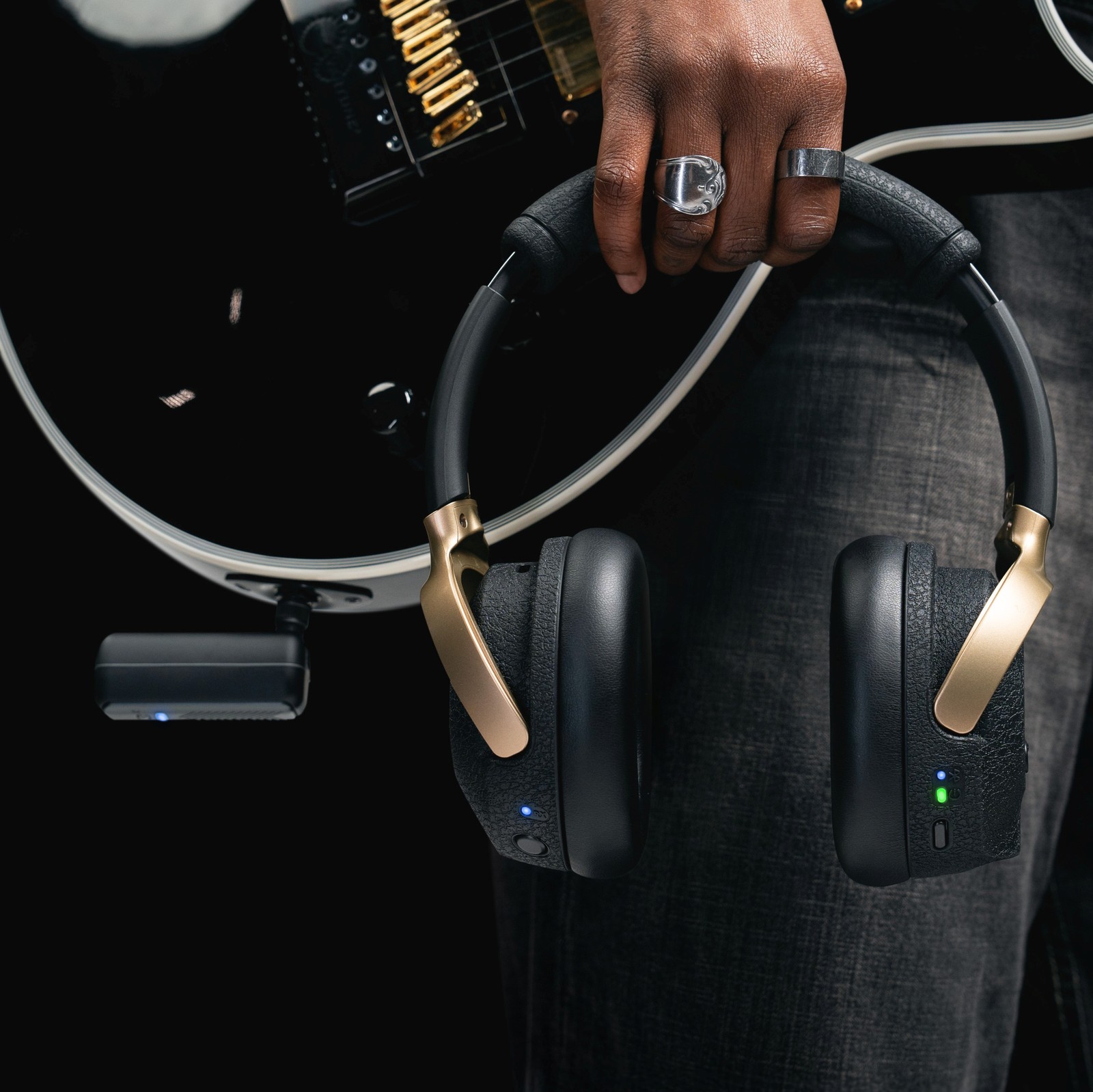 Positive Grid Spark Neo transmitter connected to a guitar and headphones held in a hand
